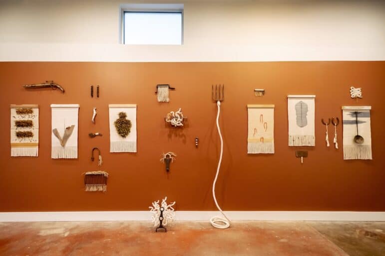 An array of wall hangings featuring natural materials, printed pigment, and cotton hang on an earth-toned wall.